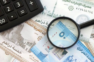 Birleşik Arap Emirlikleri kara para birimi faturaları ve büyüteçle yakınlaştırılmış hesap makinesi. Vergilendirme ve para sayımı kavramı