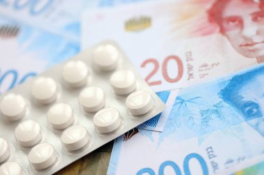 Israel New Shekels banknotları ve ilaç hapları. Mevcut İsrail para ve uyuşturucu faturaları büyük miktarda masada yatıyor. İsrail 'de ilaç ve eczane kavramı