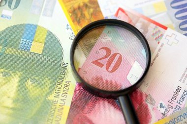 İsviçre frangı banknotları ve büyüteç. İçinde loupe olan şu anki para banknotları büyük miktarda masada yatıyor. İsviçre 'de mali izleme ve vergilendirme kavramı