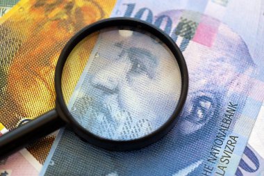 İsviçre frangı banknotları ve büyüteç. İçinde loupe olan şu anki para banknotları büyük miktarda masada yatıyor. İsviçre 'de mali izleme ve vergilendirme kavramı