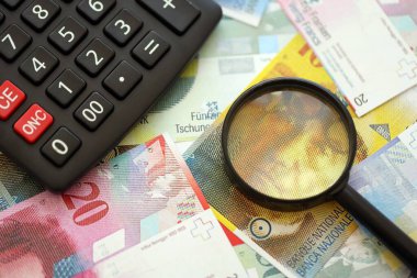 İsviçre frangı banknotları ve büyüteçli hesap makinesi. Mevcut para faturaları ve loupe ile calc büyük miktarda masada yatıyor. İsviçre 'de vergilendirme ve iş kavramı