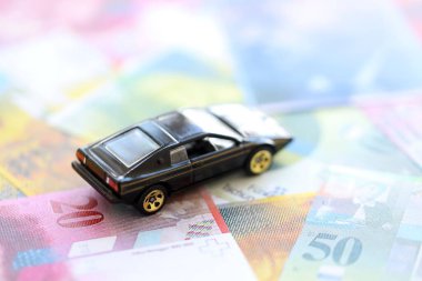 İsviçre frangı banknotları ve oyuncak araba. Mevcut frank, faturalar ve siyah araba büyük miktarda masada yatıyor. İsviçre 'de araba sahibi olma kavramı