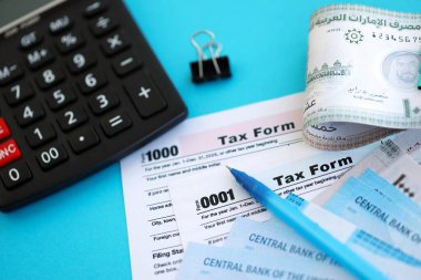 Birleşik Arap Emirlikleri kara para faturaları ve mavi üzerine yakın vergi formlu hesap makinesi. Vergi ve muhasebe kavramı