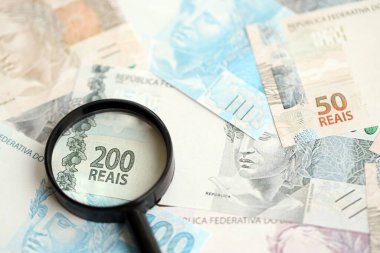 Brezilya reais banknotları ve büyüteç. Mevcut Brezilya gerçek para faturaları ve loupe büyük miktarda masada yatıyor. Brezilya 'da mali izleme ve vergilendirme kavramı