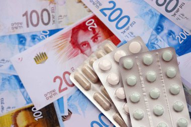 Israel New Shekels banknotları ve ilaç hapları. Mevcut İsrail para ve uyuşturucu faturaları büyük miktarda masada yatıyor. İsrail 'de ilaç ve eczane kavramı