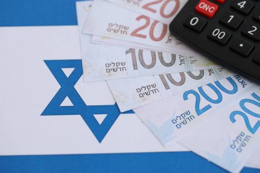 Israel New Shekels banknotları ve hesap makinesi bayrağın üzerinde. İsrail 'in mevcut para faturaları ve kalibreleri büyük oranda bayrakta yatıyor. İsrail 'de vergilendirme ve para kavramı