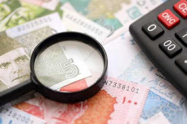 Pakistan banknotları ve büyüteçle hesap makinesi. Mevcut Pakistan para faturaları ve loupe ile calc büyük miktarda masada yatıyor. Pakistan 'da vergi ve para sayımı kavramı
