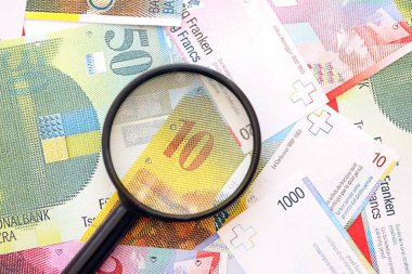 İsviçre frangı banknotları ve büyüteç. İçinde loupe olan şu anki para banknotları büyük miktarda masada yatıyor. İsviçre 'de mali izleme ve vergilendirme kavramı