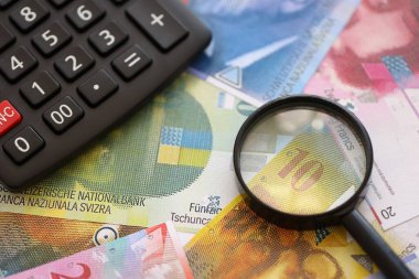 İsviçre frangı banknotları ve büyüteçli hesap makinesi. Mevcut para faturaları ve loupe ile calc büyük miktarda masada yatıyor. İsviçre 'de vergilendirme ve iş kavramı