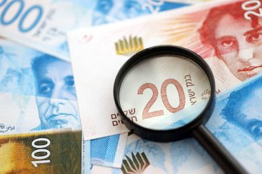 Israel New Shekels banknotları ve büyüteç. Şu anki İsrail 'in yüksek meblağlı faturaları masanın üzerinde yatıyor. İsrail 'de mali izleme ve vergilendirme kavramı
