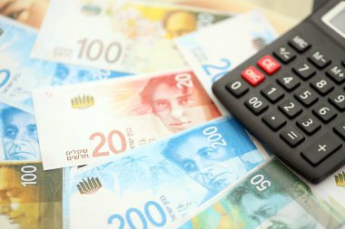 Israel New Shekels banknotları ve hesap makinesi. Mevcut İsrail para faturaları ve kalibreleri büyük miktarda masada yatıyor. İsrail 'de vergilendirme ve para kavramı