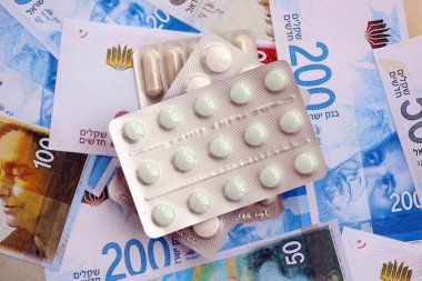 Israel New Shekels banknotları ve ilaç hapları. Mevcut İsrail para ve uyuşturucu faturaları büyük miktarda masada yatıyor. İsrail 'de ilaç ve eczane kavramı