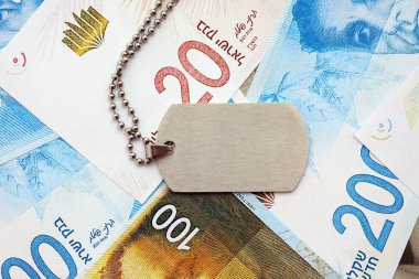 İsrail Yeni Şekelleri 'nin banknotları ve askeri simgesi. İsrail 'in mevcut para faturaları ve künyeleri büyük miktarda masada yatıyor. İsrail 'de askerlik kavramı