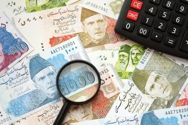 Pakistan banknotları ve büyüteçle hesap makinesi. Mevcut Pakistan para faturaları ve loupe ile calc büyük miktarda masada yatıyor. Pakistan 'da vergi ve para sayımı kavramı