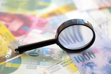 İsviçre frangı banknotları ve büyüteç. İçinde loupe olan şu anki para banknotları büyük miktarda masada yatıyor. İsviçre 'de mali izleme ve vergilendirme kavramı