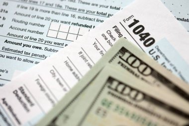 Yüz dolarlık banknotlar ve 1040 bireysel gelir vergisi iade formu yakın çekim. Çok az Amerikan doları ve Birleşik Devletler vergisi yok. ABD 'de vergi ödeme ve muhasebe kavramı