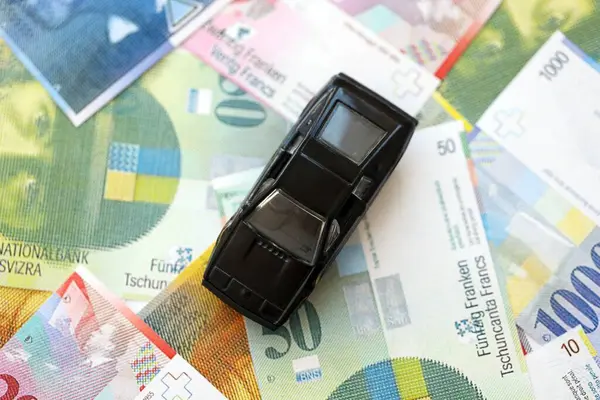 İsviçre frangı banknotları ve oyuncak araba. Mevcut frank, faturalar ve siyah araba büyük miktarda masada yatıyor. İsviçre 'de araba sahibi olma kavramı