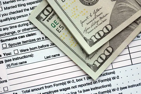 Yüz dolarlık banknotlar ve 1040 bireysel gelir vergisi iade formu yakın çekim. Çok az Amerikan doları ve Birleşik Devletler vergisi yok. ABD 'de vergi ödeme ve muhasebe kavramı