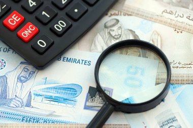 Birleşik Arap Emirlikleri kara para birimi faturaları ve büyüteçle yakınlaştırılmış hesap makinesi. Vergilendirme ve para sayımı kavramı