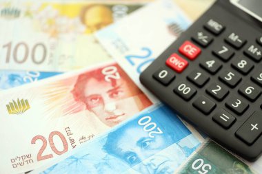Israel New Shekels banknotları ve hesap makinesi. Mevcut İsrail para faturaları ve kalibreleri büyük miktarda masada yatıyor. İsrail 'de vergilendirme ve para kavramı