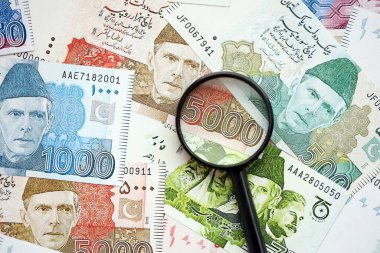 Pakistan banknotları ve büyüteç. Pakistan 'ın mevcut para ve büyüteç faturaları büyük miktarda masanın üzerinde duruyor. Pakistan 'da mali izleme ve vergilendirme kavramı
