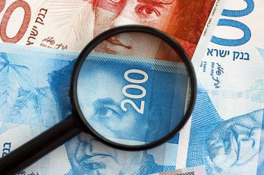 Israel New Shekels banknotları ve büyüteç. Şu anki İsrail 'in yüksek meblağlı faturaları masanın üzerinde yatıyor. İsrail 'de mali izleme ve vergilendirme kavramı