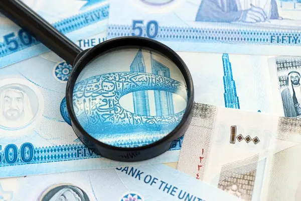 Birleşik Arap Emirlikleri kara para birimi banknotları ve büyüteç yakın çekim. Finansal izleme ve vergilendirme kavramı