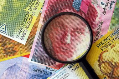 İsviçre frangı banknotları ve büyüteç. İçinde loupe olan şu anki para banknotları büyük miktarda masada yatıyor. İsviçre 'de mali izleme ve vergilendirme kavramı