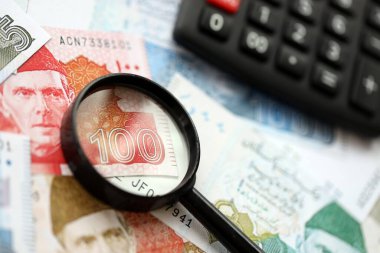 Pakistan banknotları ve büyüteçle hesap makinesi. Mevcut Pakistan para faturaları ve loupe ile calc büyük miktarda masada yatıyor. Pakistan 'da vergi ve para sayımı kavramı
