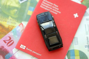 İsviçre frangı banknotları ve pasaportlu oyuncak araba. Mevcut frank, faturalar ve geçiş kartı olan siyah araba büyük miktarda masada yatıyor. İsviçre 'de araba sahibi olma kavramı