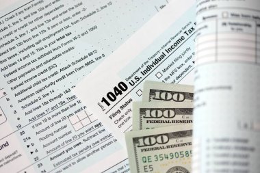 Yüz dolarlık banknotlar ve 1040 bireysel gelir vergisi iade formu yakın çekim. Çok az Amerikan doları ve Birleşik Devletler vergisi yok. ABD 'de vergi ödeme ve muhasebe kavramı