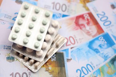 Israel New Shekels banknotları ve ilaç hapları. Mevcut İsrail para ve uyuşturucu faturaları büyük miktarda masada yatıyor. İsrail 'de ilaç ve eczane kavramı