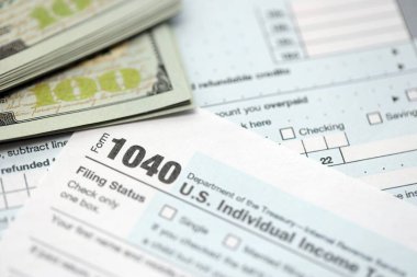 Yüz dolarlık banknotlar ve 1040 bireysel gelir vergisi iade formu yakın çekim. Çok az Amerikan doları ve Birleşik Devletler vergisi yok. ABD 'de vergi ödeme ve muhasebe kavramı