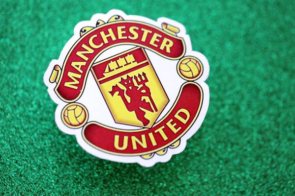 КИЕВ, УКРАИНА - 23 февраля 2025 года значок футбольного клуба "Манчестер Юнайтед" на фоне изумрудно-зеленого блеска