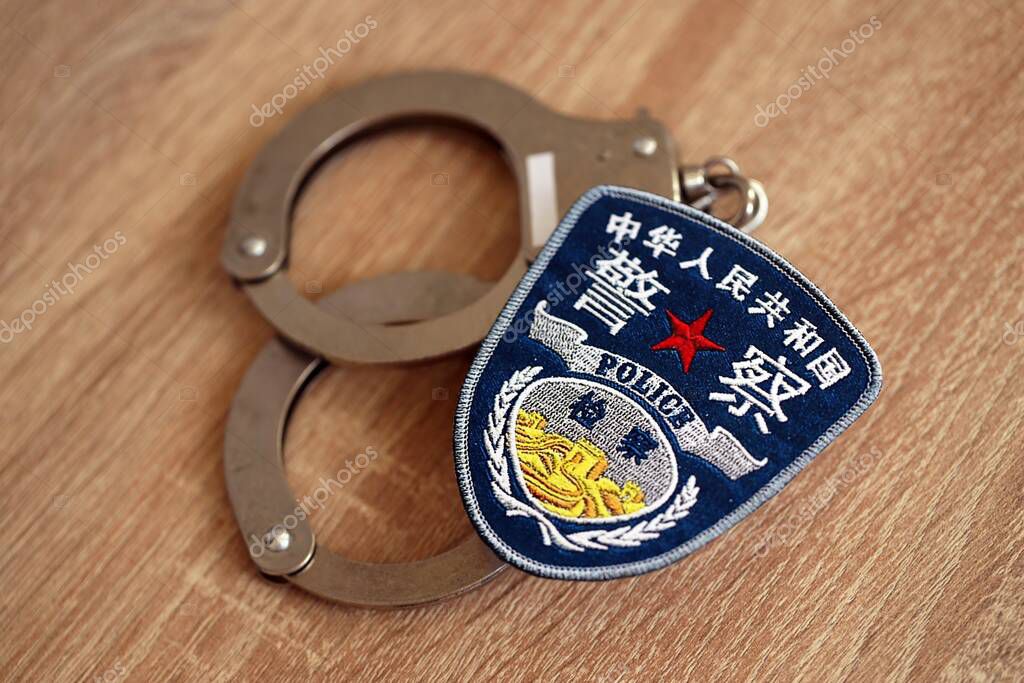 KYIV, UKRAINE - SEPTEMBER 17, 2025 Chinese Police badge with handcuffs on wooden table close up