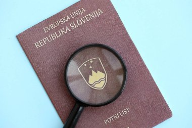 Slovenya pasaportu ve açık mavi kağıtta büyüteç yakın plan. Vatandaşlık detayları ve bilgi kavramı