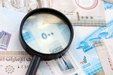 Birleşik Arap Emirlikleri kara para birimi banknotları ve büyüteç yakın çekim. Finansal izleme ve vergilendirme kavramı