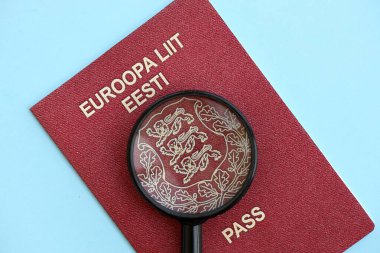 Açık mavi kağıtta Estonya pasaportu ve büyüteç yakın plan. Vatandaşlık detayları ve bilgi kavramı