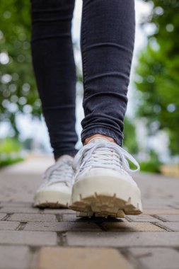 Siyah kotlu kadın bacaklarında çivili tabanlı beyaz spor ayakkabılar.