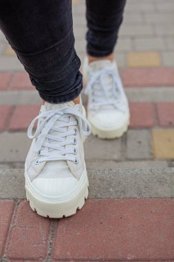 Siyah kotlu kadın bacaklarında çivili tabanlı beyaz spor ayakkabılar.