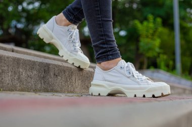 Siyah kotlu kadın bacaklarında çivili tabanlı beyaz spor ayakkabılar.