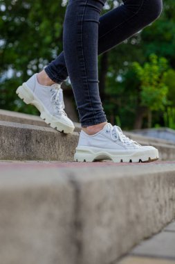 Siyah kotlu kadın bacaklarında çivili tabanlı beyaz spor ayakkabılar.