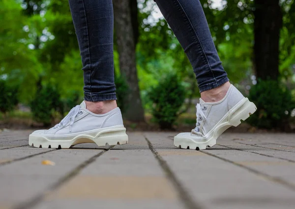 Siyah kotlu kadın bacaklarında çivili tabanlı beyaz spor ayakkabılar.