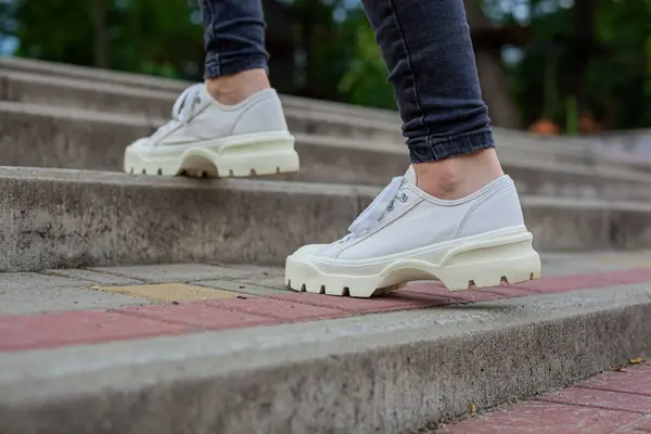 Siyah kotlu kadın bacaklarında çivili tabanlı beyaz spor ayakkabılar.