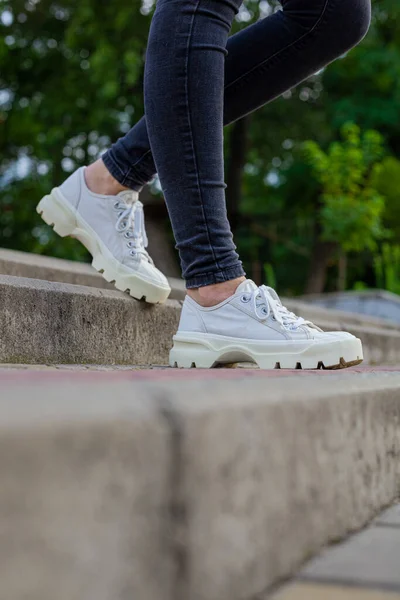 Siyah kotlu kadın bacaklarında çivili tabanlı beyaz spor ayakkabılar.