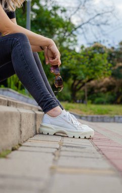 Kız merdivenlerde oturuyor ve elinde güneş gözlüğü tutuyor.