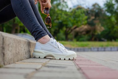 Kız merdivenlerde oturuyor ve elinde güneş gözlüğü tutuyor.