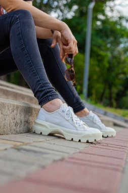 Kız merdivenlerde oturuyor ve elinde güneş gözlüğü tutuyor.