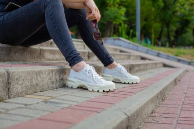 Kız merdivenlerde oturuyor ve elinde güneş gözlüğü tutuyor.