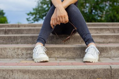 Kız merdivenlerde oturuyor ve elinde güneş gözlüğü tutuyor.